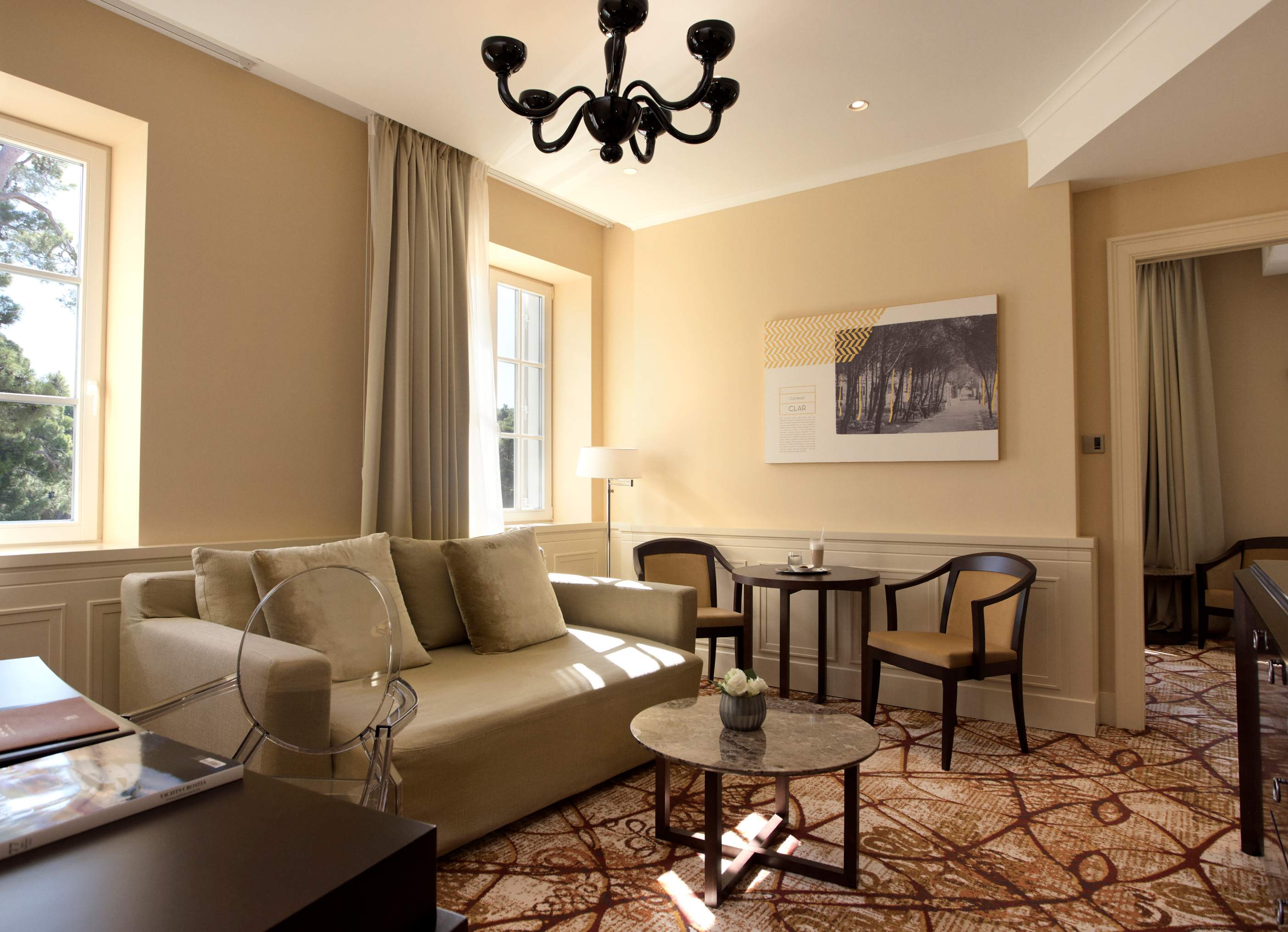 An elegant living room with a beige sofa, a round marble coffee table, modern chairs, and a large window with curtains