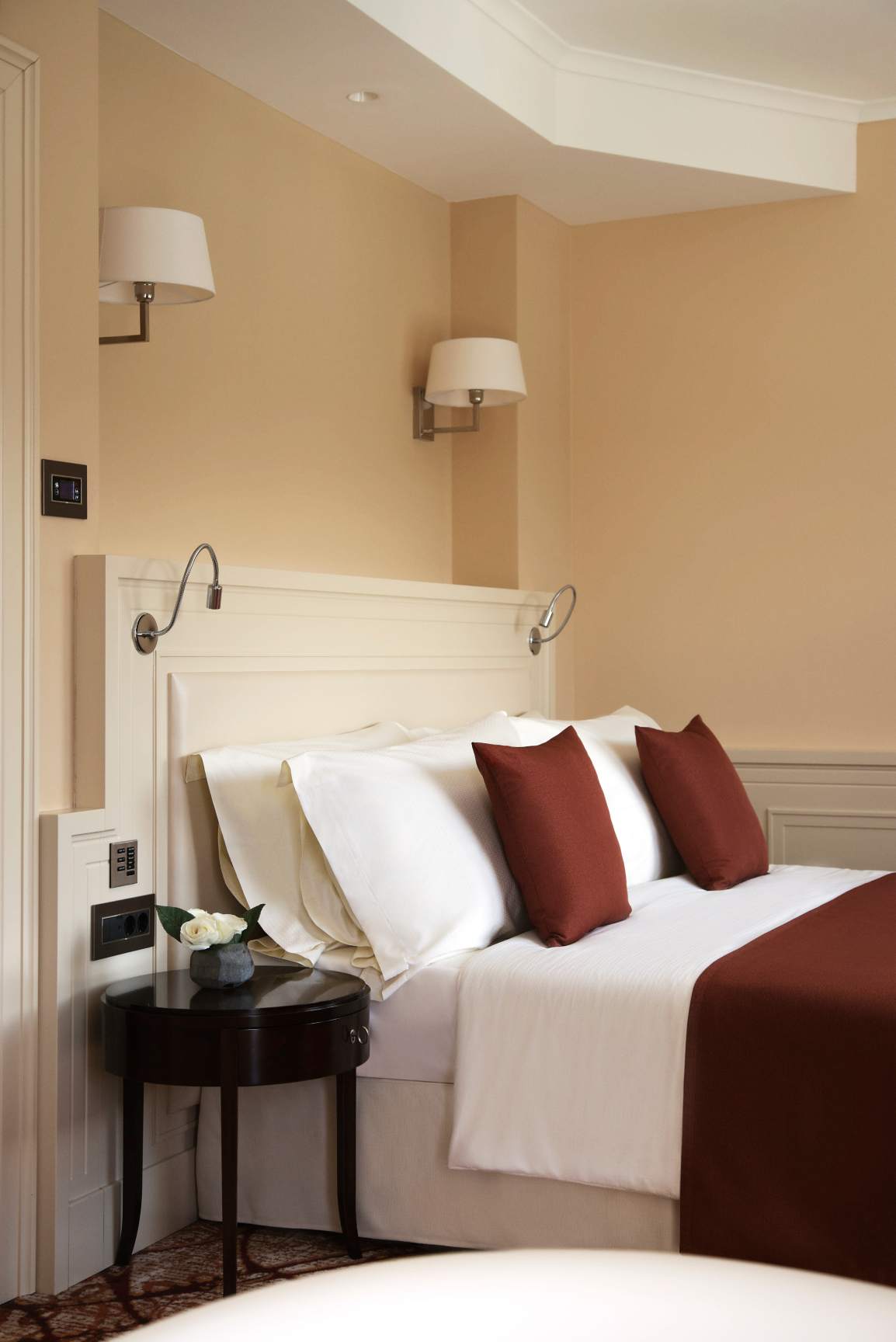 Neatly made bed with white linens and brown accent pillows in a warmly lit, elegant room