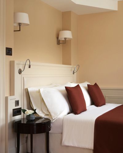 Neatly made bed with white linens and brown accent pillows in a warmly lit, elegant room