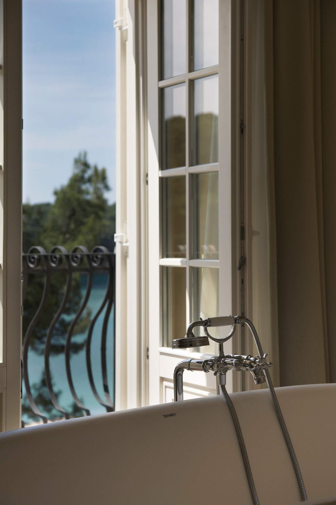 Close-up of a classic bathtub faucet with a partial view of a balcony and trees through an open window