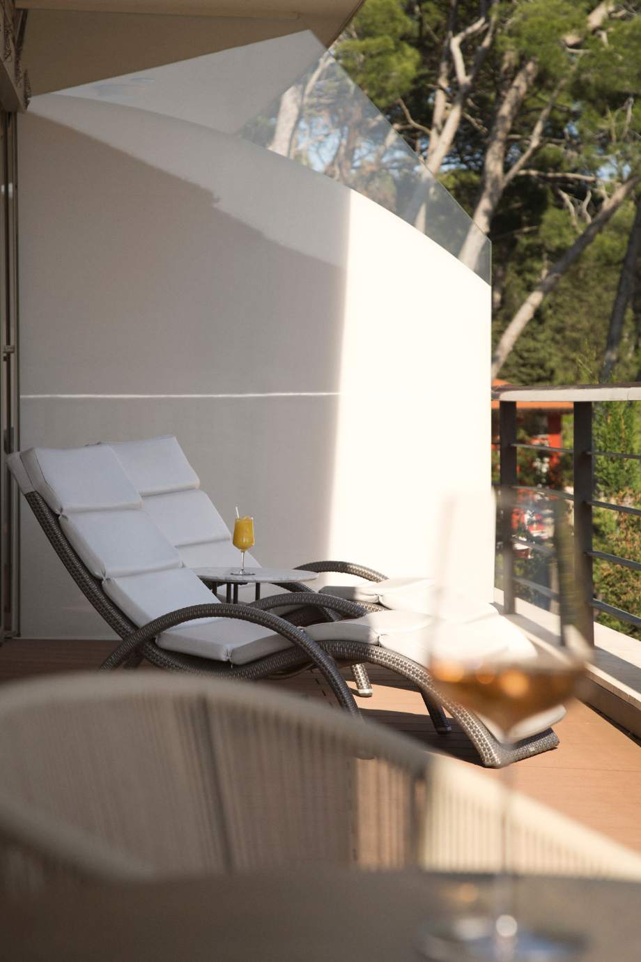 Sunlit terrace with a reclining lounge chair and a small table, set against a backdrop of trees and a clear sky