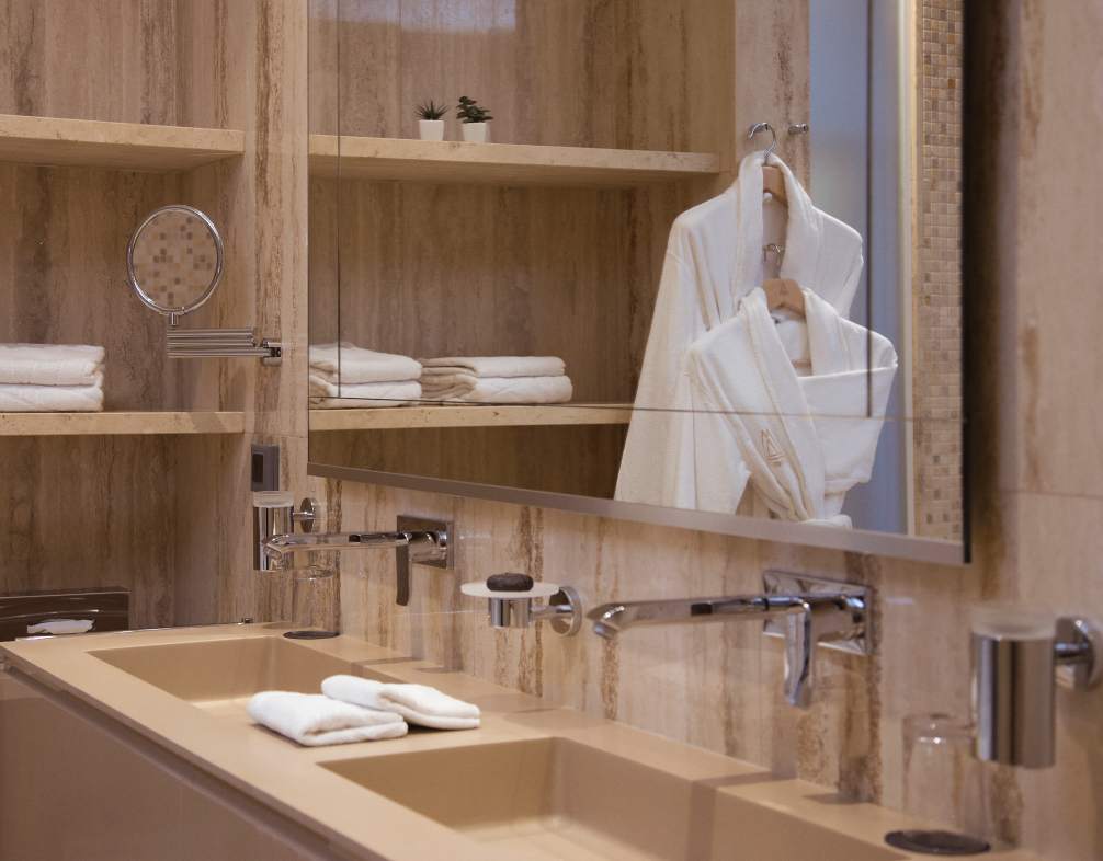 A refined bathroom interior with a sleek beige sink, a large mirror reflecting plush towels and a bathrobe, accented by wooden shelving