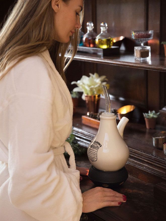 Woman in a spa robe preparing a personal inhalation treatment with a ceramic inhaler on a wooden bar