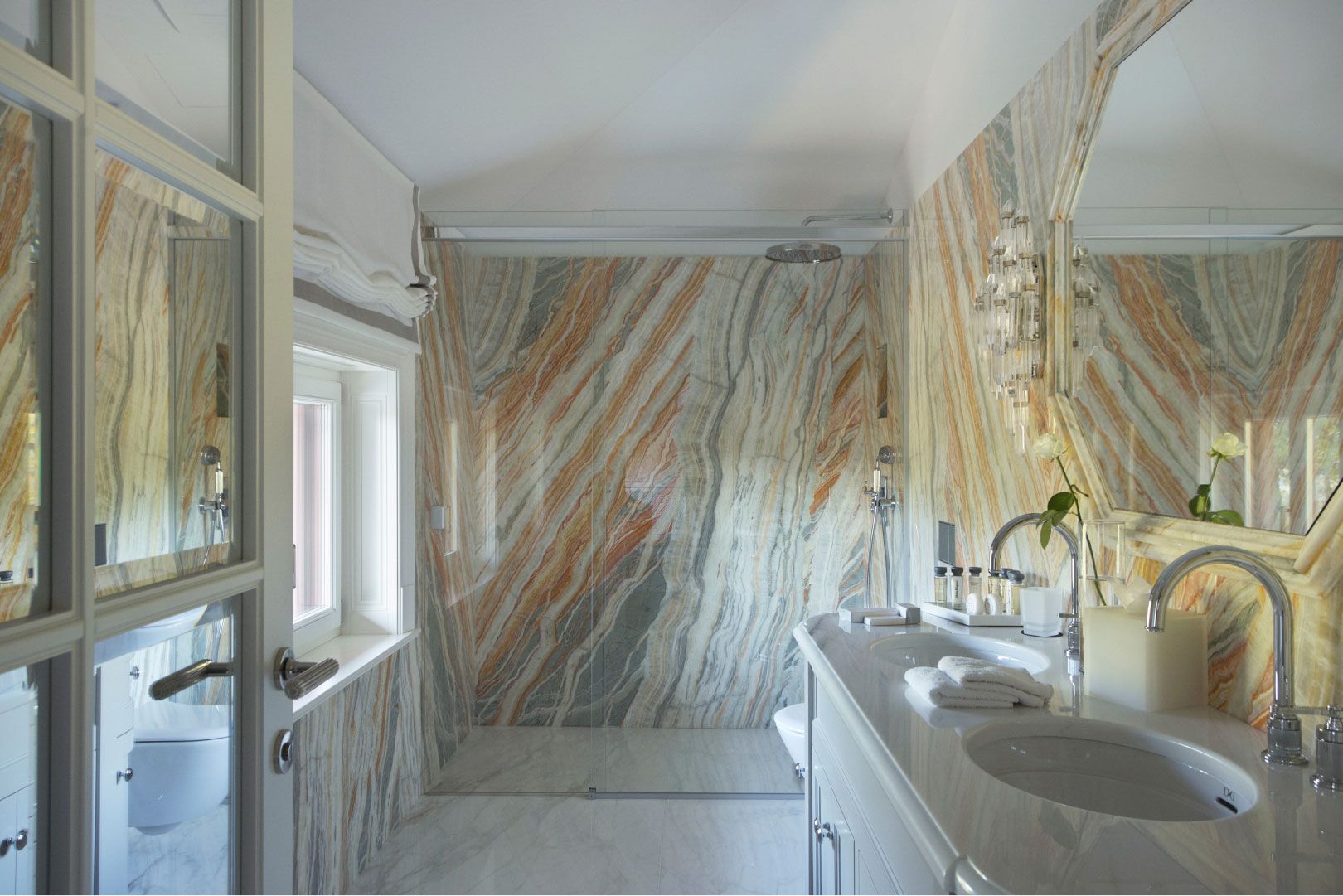 A luxurious bathroom adorned with striking marble walls and floors, featuring a sleek double sink vanity and a spacious walk-in shower