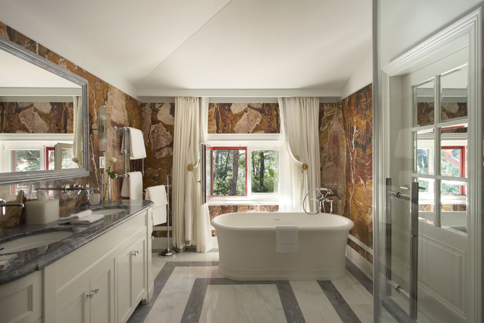 A serene bathroom with a freestanding bathtub, elegant marble accents, and a window offering a view of nature, creating a luxurious and tranquil space