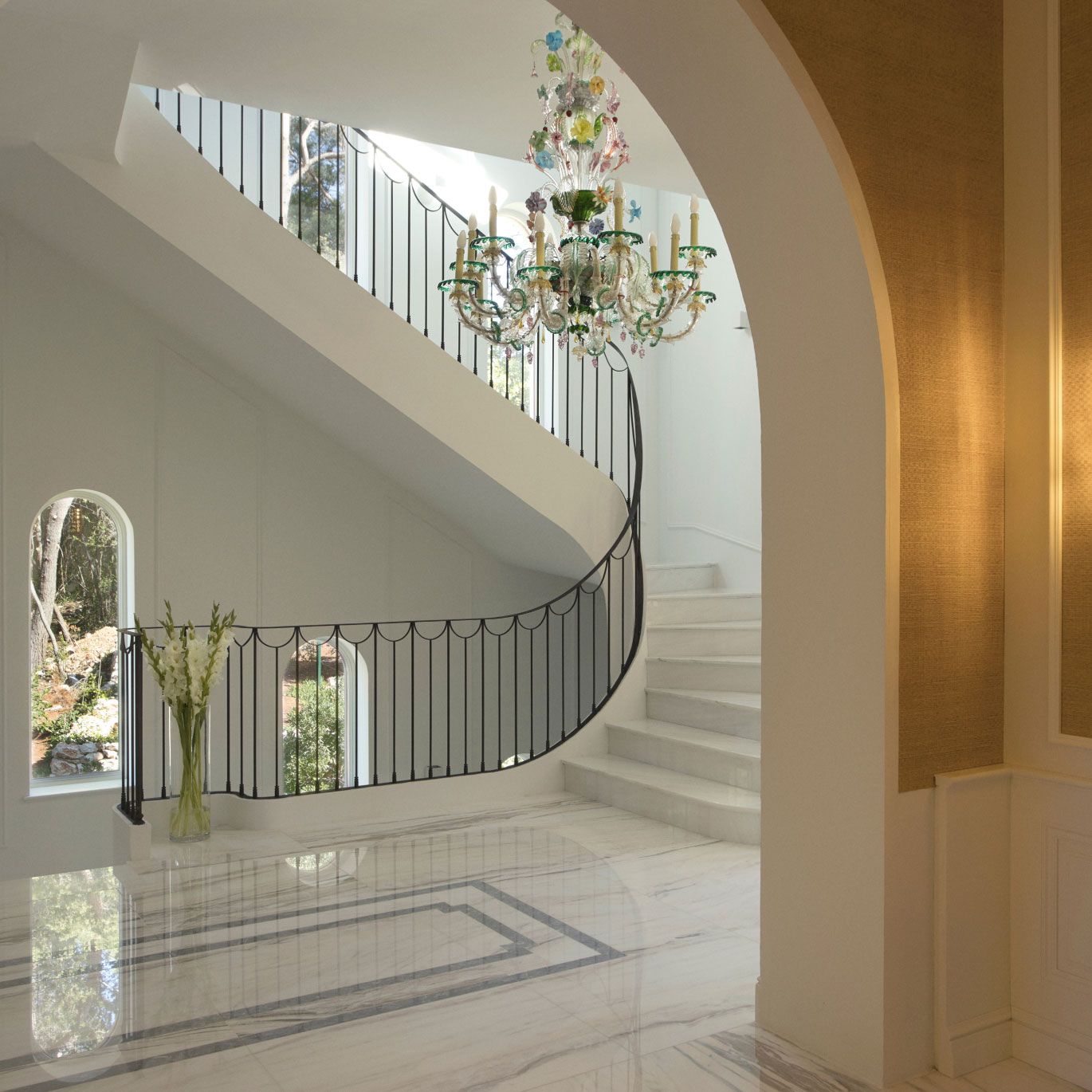 A grand foyer with a sweeping curved staircase, elegant marble floors, and a luxurious, colorful chandelier creating a welcoming and opulent entrance