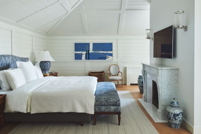 An inviting bedroom with a vaulted ceiling, featuring a classic fireplace, white walls, and blue and white decor accents.