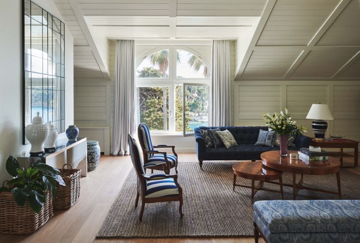 A serene and stylish living room with natural light pouring in through large windows, showcasing comfortable blue sofas, wooden furniture, and a view of palm trees outside.