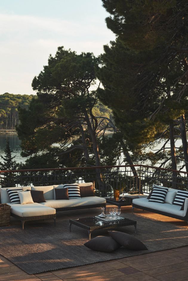 Black and white modern couch on a sunny deck overlooks a calm lake framed by greenery.