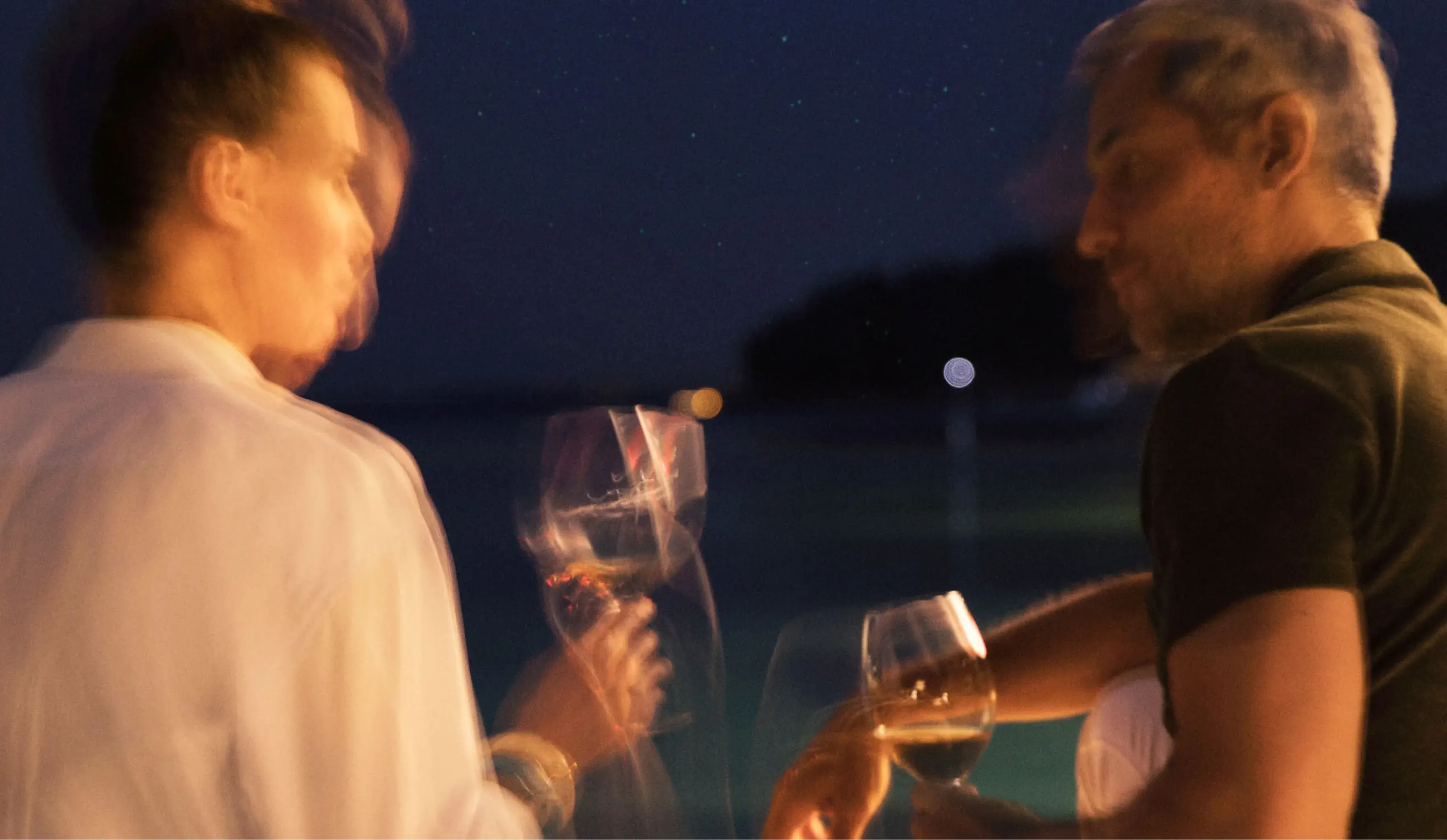 Two people enjoying glasses of wine under a starry sky, in a blurred, dreamy setting