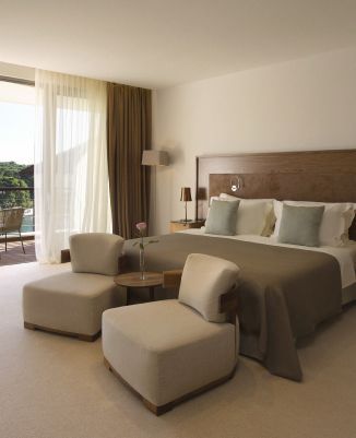 A well-appointed luxury suite with a comfortable bed, armchairs, and a glass door leading to a balcony with a view